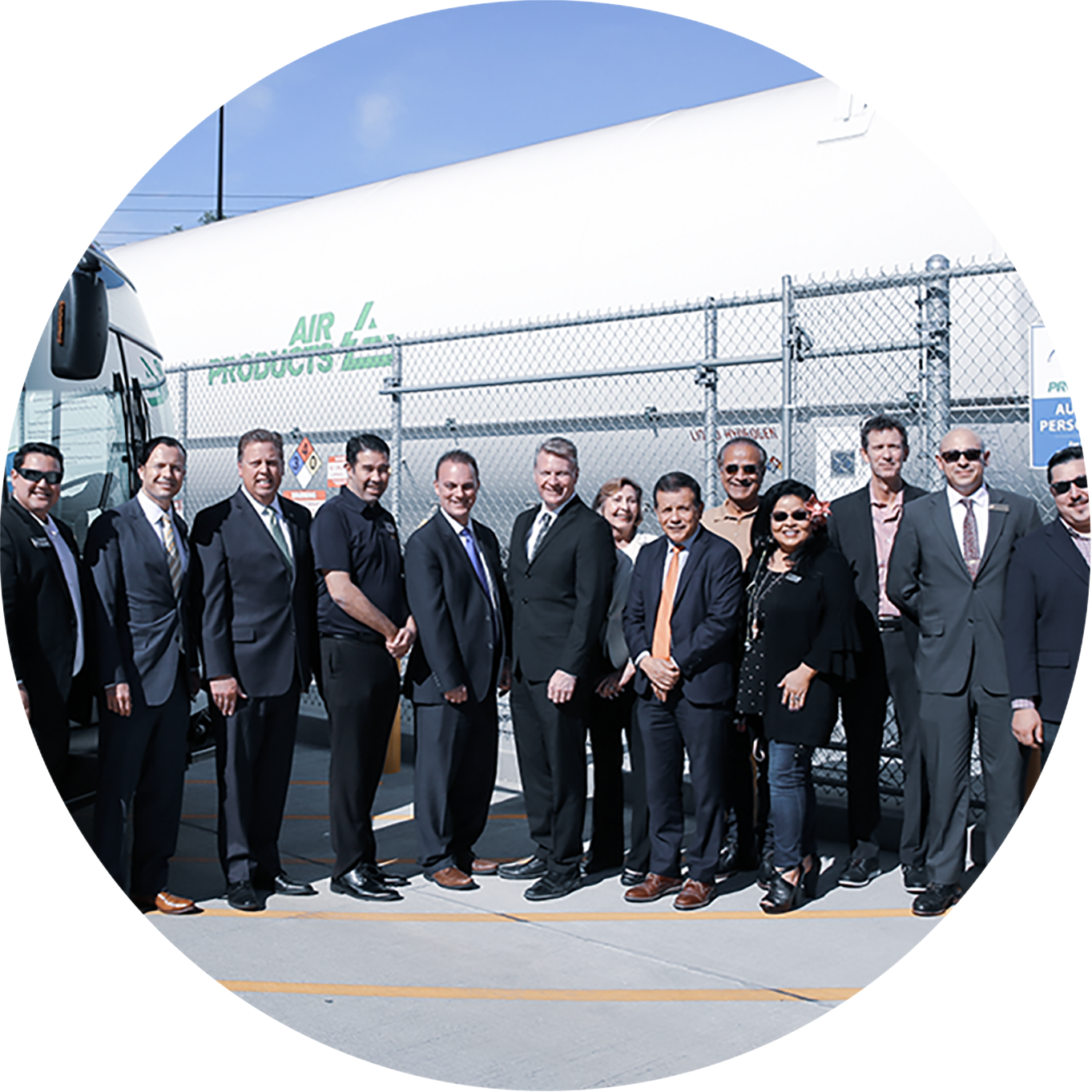 a group of people in suits and ties standing in front of a fenced building with a sign that says air products