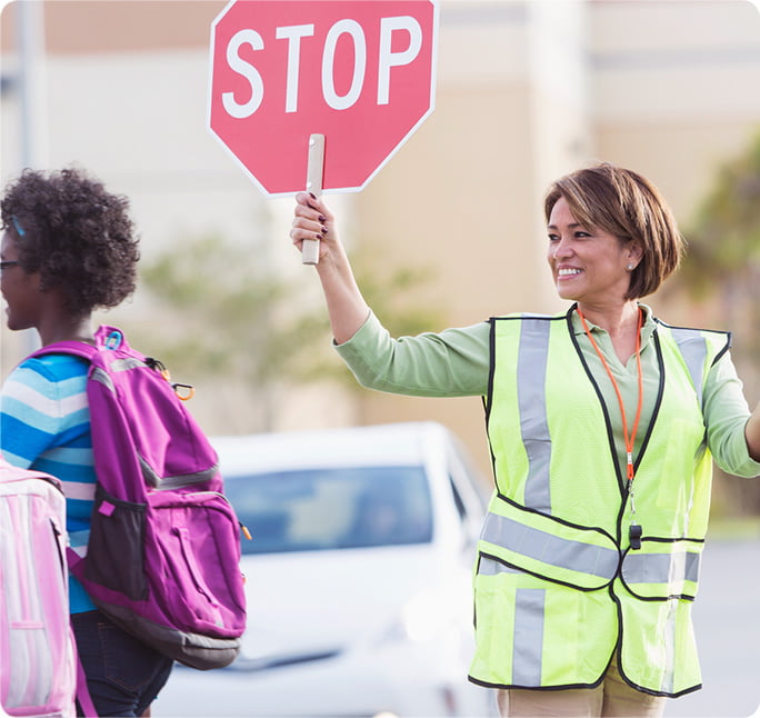 A woman with a hand-held stop sign helps students cross the street safely